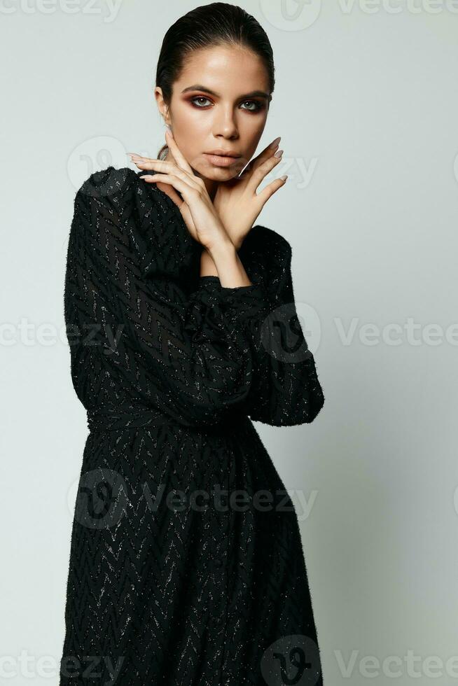 ziemlich Frau halten Hände in der Nähe von Gesicht schwarz Kleid attraktiv aussehen Studio foto