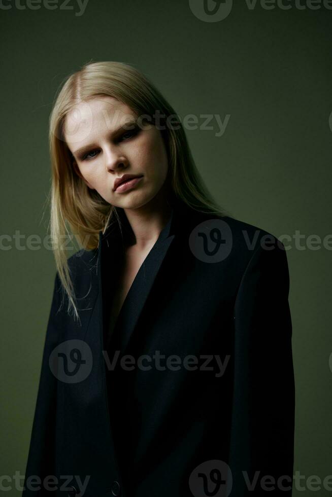 blond sieht aus Über ihr Schulter im ein schwarz Jacke posieren halb gedreht im das Studio auf ein Grün Hintergrund. das Konzept von stilvoll Mode Fotografie foto