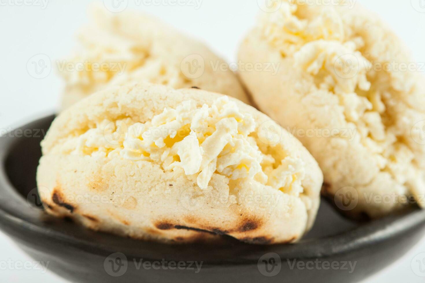 kolumbianisch traditionell Weiß Mais Arepa ausgestopft mit gerieben Käse im ein schwarz Keramik Gericht auf Weiß Hintergrund foto