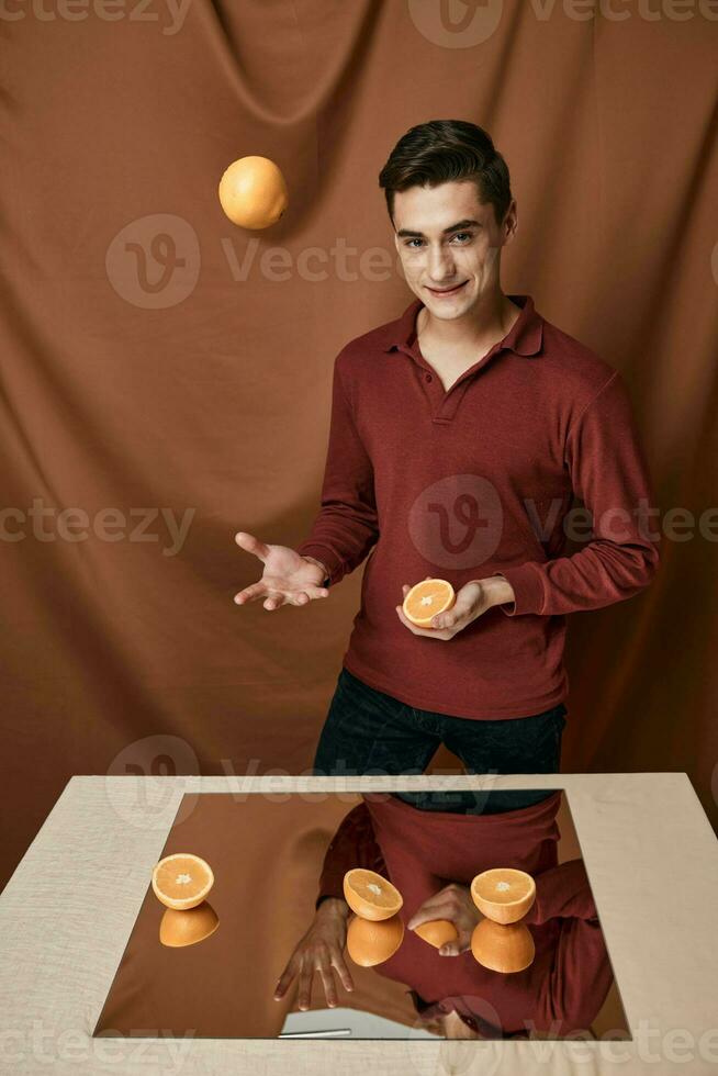 ein gut aussehend Mann wirft ein Orange in der Nähe von das Tabelle mit ein Spiegel foto