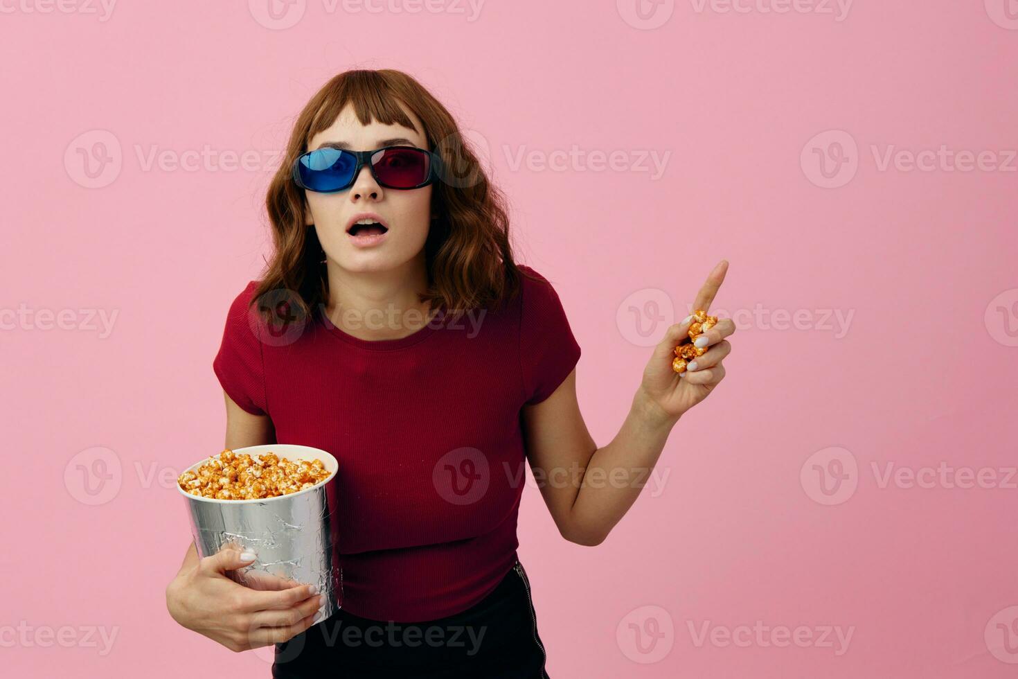 verwirrt konzentriert süß Rothaarige Dame im rot T-Shirt 3d Brille Essen Popcorn Uhr Film posieren isoliert auf Über Rosa Studio Hintergrund. Kopieren Raum Banner. Mode Kino Konzept. Unterhaltung Angebot foto