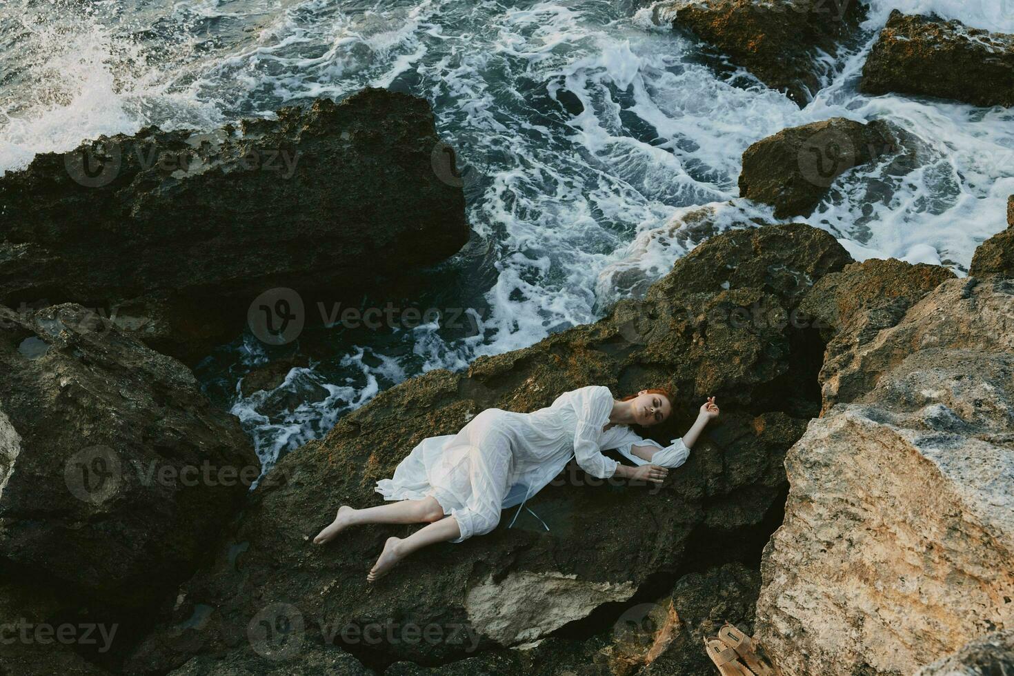 schön Braut im lange Weiß Kleid nass Haar Lügen auf ein felsig Cliff Sommer- Ferien Konzept foto