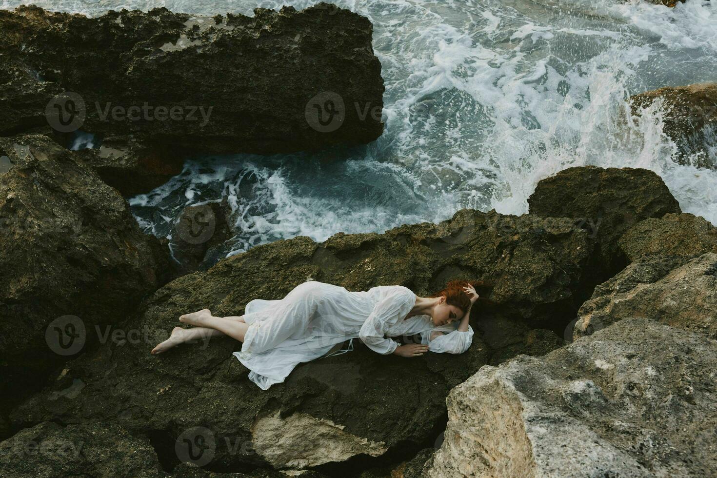 schön Frau im lange Weiß Kleid nass Haar Lügen auf ein felsig Cliff Natur Landschaft foto