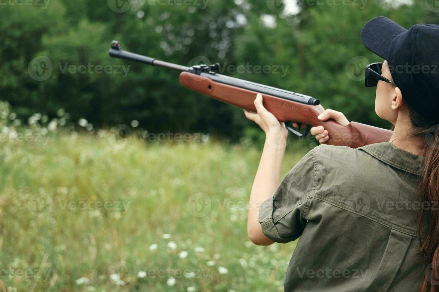 Frau auf draussen halten ein Gewehr in der Nähe von seine Kopf Sicht Jagd Grün Blätter foto