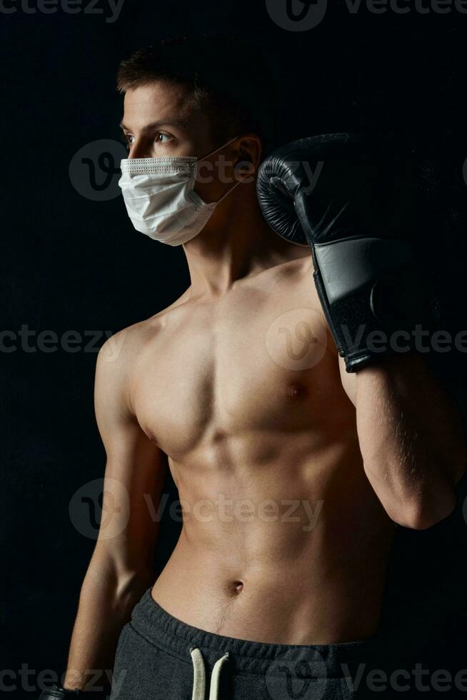 Athlet im ein medizinisch Maske Coronavirus schwarz Hintergrund Boxen Handschuhe Fitness foto