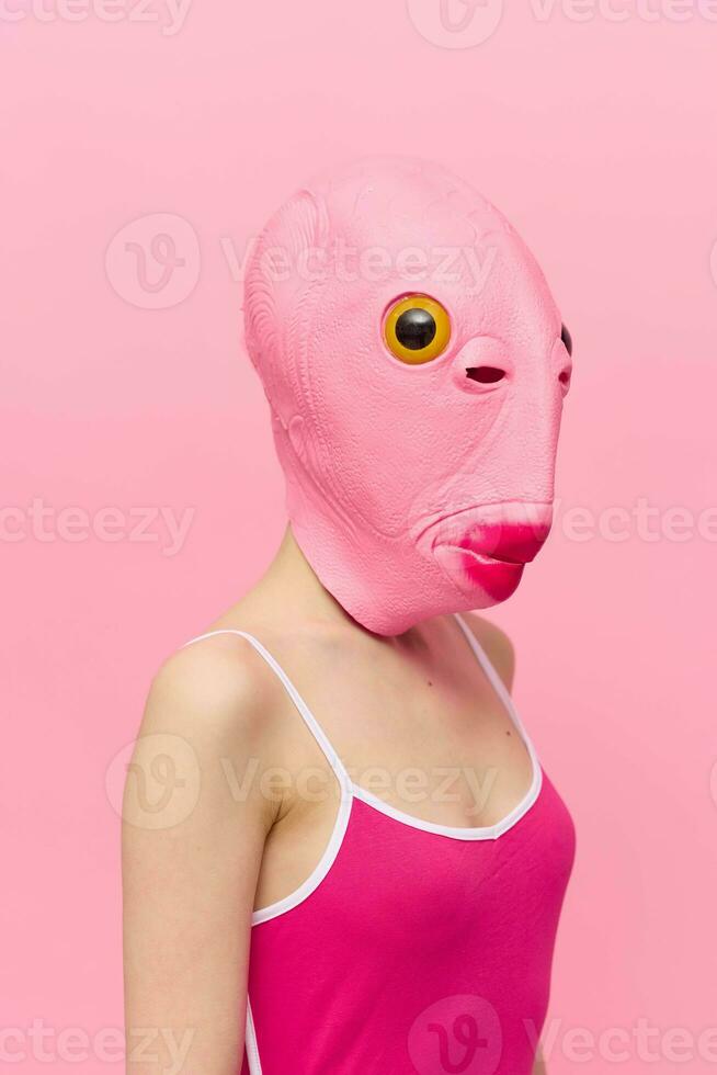 komisch verrückt Frau auf ein Rosa Hintergrund Stehen im ein Fisch Kopf Maske auf ein Rosa Hintergrund, konzeptionelle Halloween Kostüm Kunst Foto