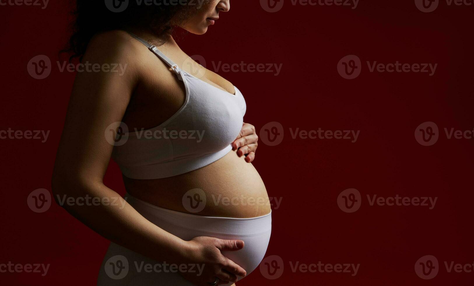 jung schwanger Frau im Weiß Unterwäsche, streicheln ihr Bauch, isoliert auf rot Hintergrund. Weiblichkeit Nacktheit Schwangerschaft foto