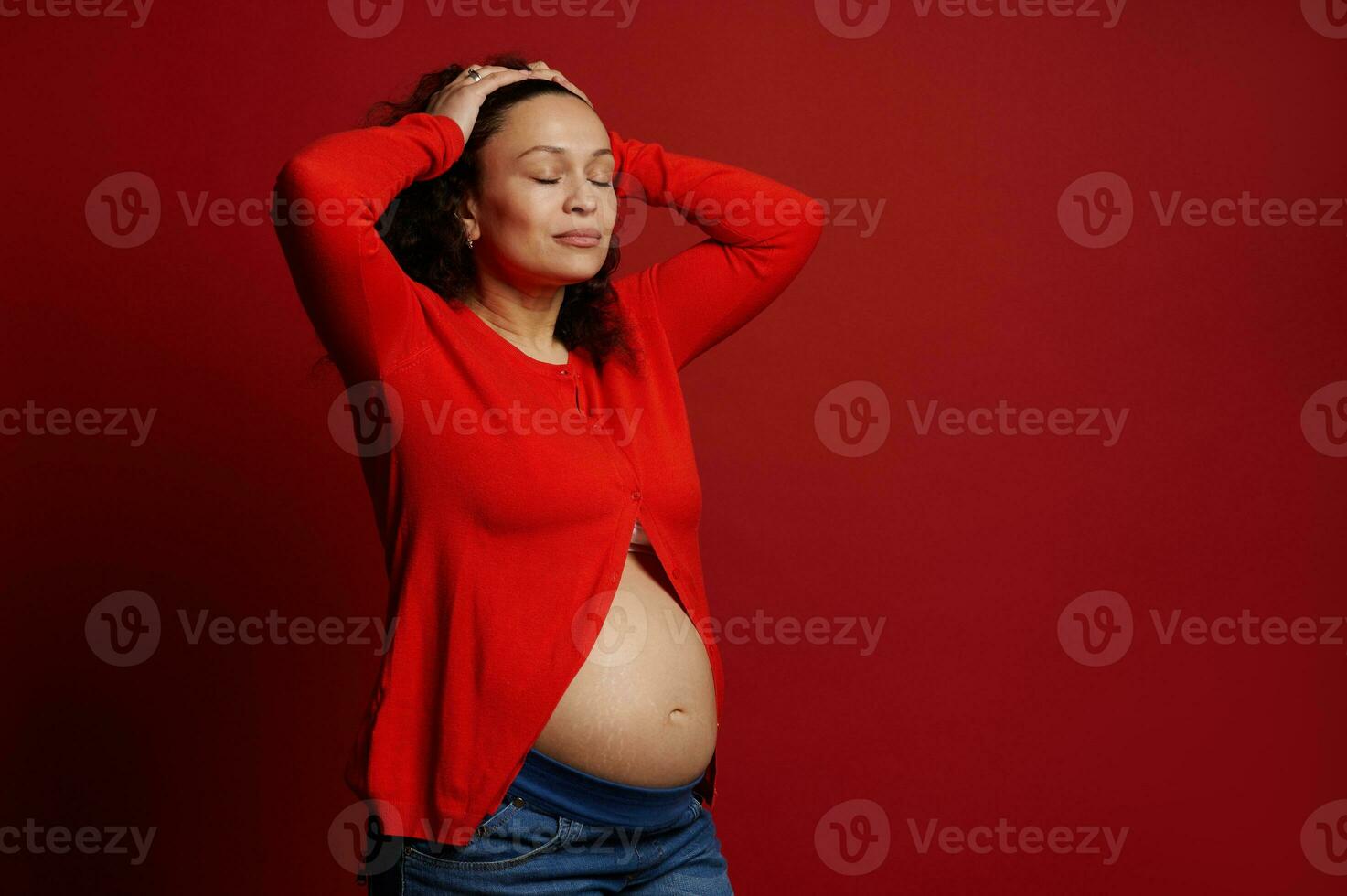 herrlich schwanger Frau posieren mit geschlossen Augen und nackt Bauch auf rot Hintergrund. glücklich Mütter Tag. Schwangerschaft. foto