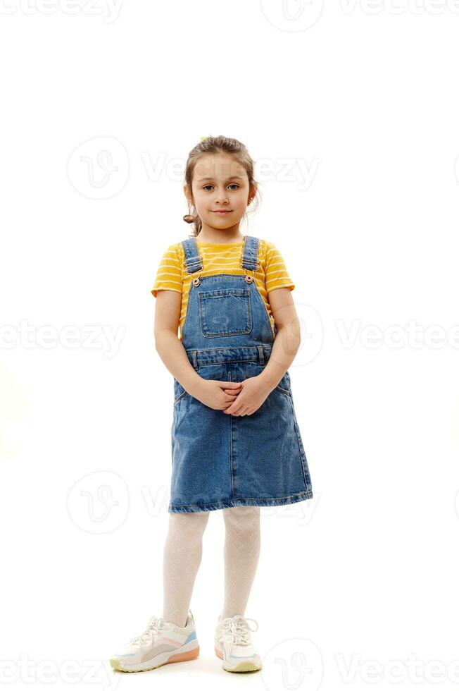 voll Länge Porträt von ein schön wenig Kind Mädchen im Denim Kleidung, suchen beim Kamera isoliert Über Weiß Hintergrund foto