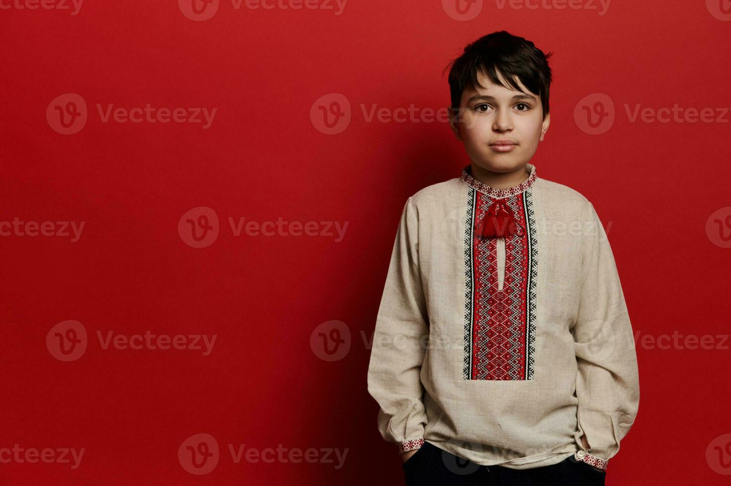 kaukasisch Teen Junge tragen Leinen- Hemd mit gestickt Ornament im ukrainisch Stil, suchen beim Kamera, isoliert auf rot foto