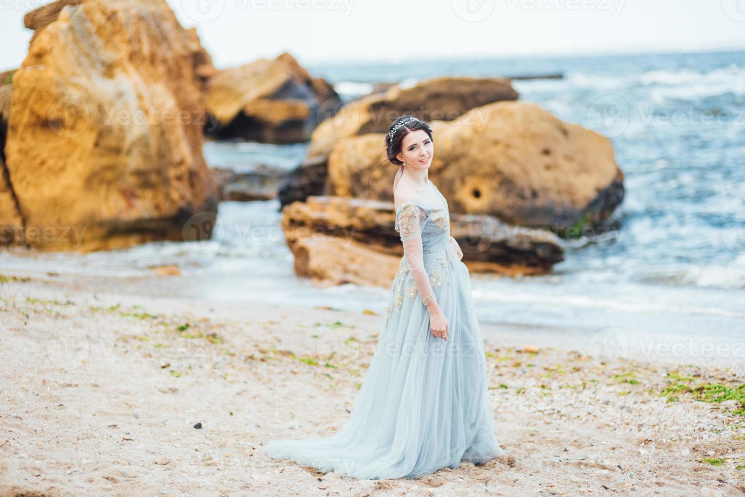 Braut in einem Blaulichtkleid, das entlang des Ozeans geht foto