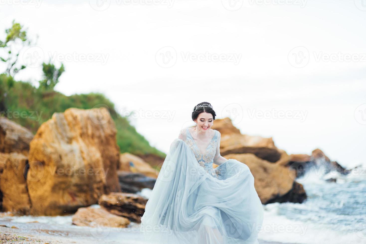 Braut in einem Blaulichtkleid, das entlang des Ozeans geht foto