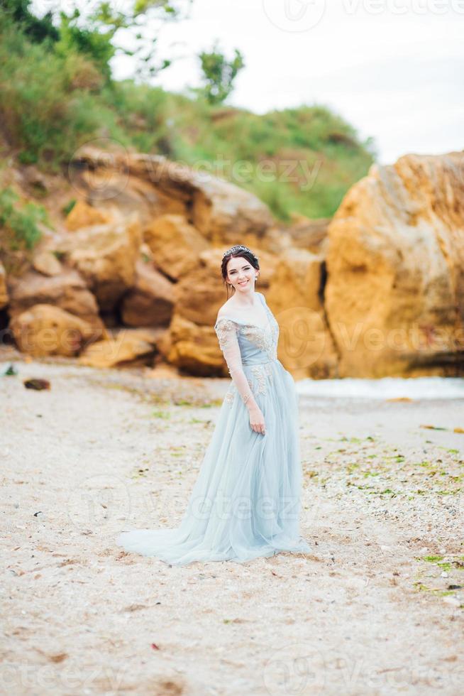 Braut in einem Blaulichtkleid, das entlang des Ozeans geht foto