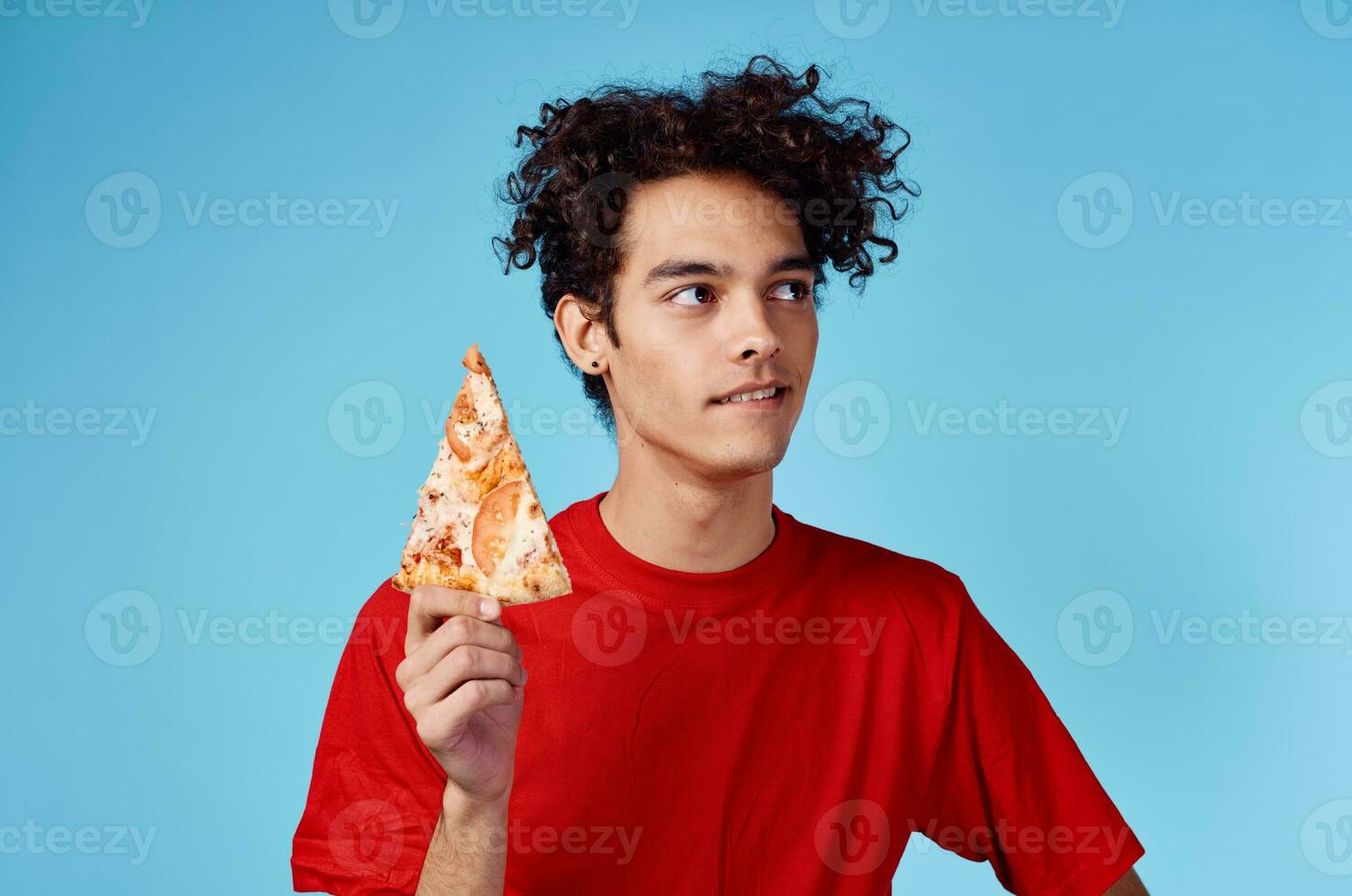 energisch Kerl mit ein Scheibe von Pizza haben Spaß auf ein Blau Hintergrund und ein rot T-Shirt foto