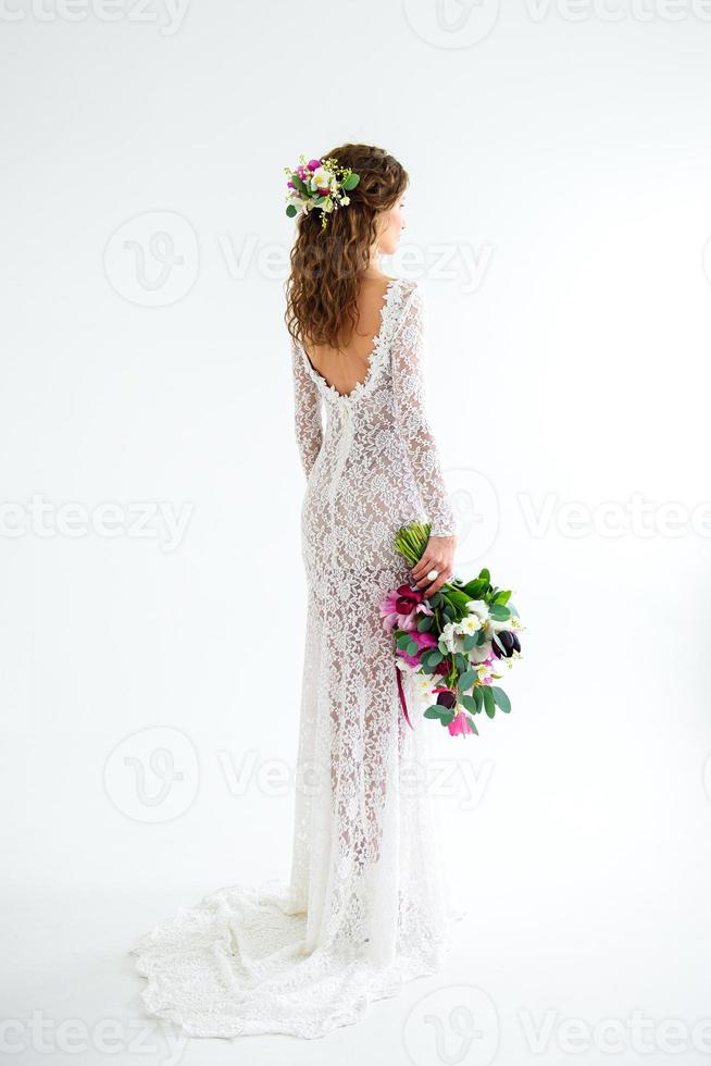 freudige Mädchenbraut in einem weißen Strickkleid, das mit einem Blumenstrauß aufwirft foto