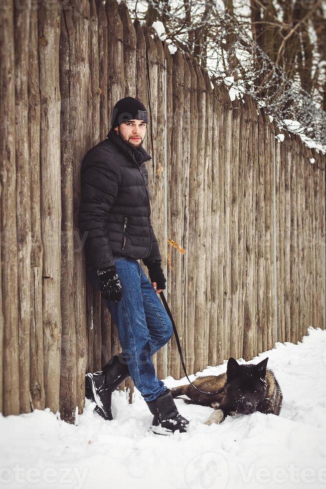 Ein Mann in einer Jacke und einer Strickmütze geht mit einem amerikanischen Akita-Hund spazieren foto