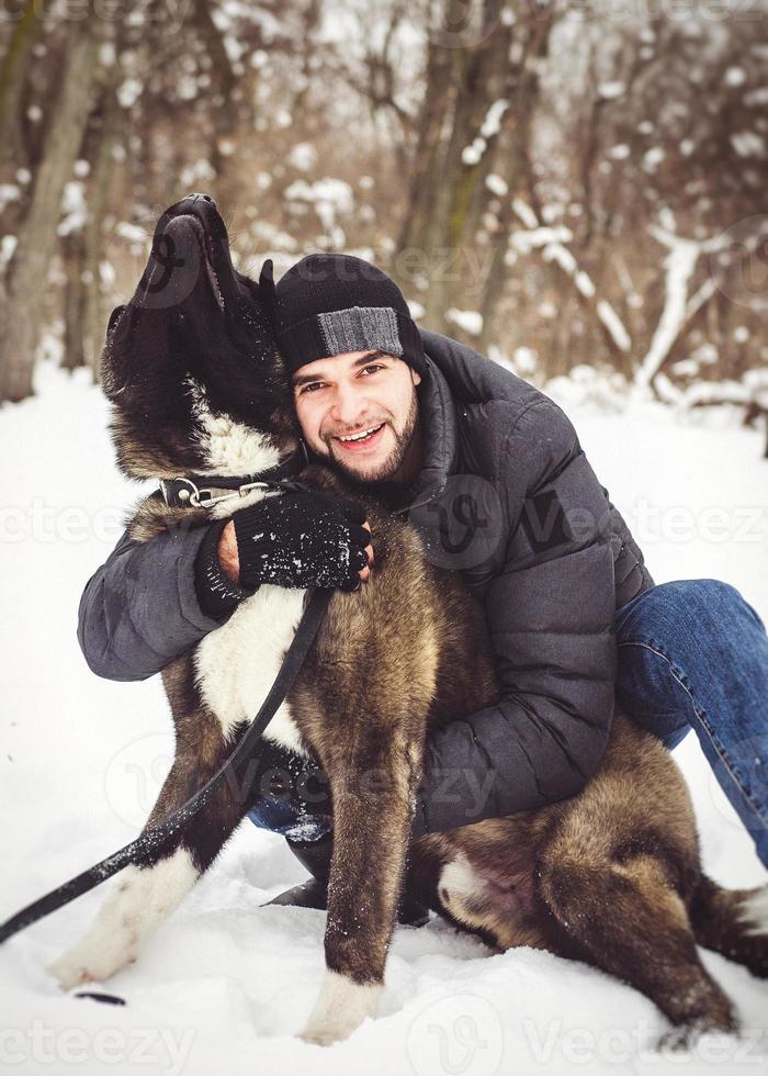 Ein Mann in einer Jacke und einer Strickmütze geht mit einem amerikanischen Akita-Hund spazieren foto