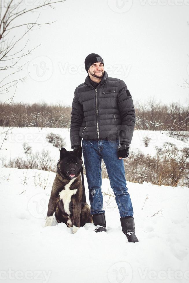 Ein Mann in einer Jacke und einer Strickmütze geht mit einem amerikanischen Akita-Hund spazieren foto