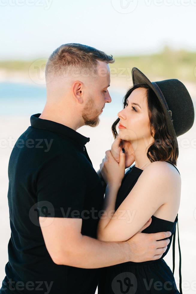 junges Paar ein Mann mit einem Mädchen in schwarzen Kleidern geht auf dem weißen Sand foto