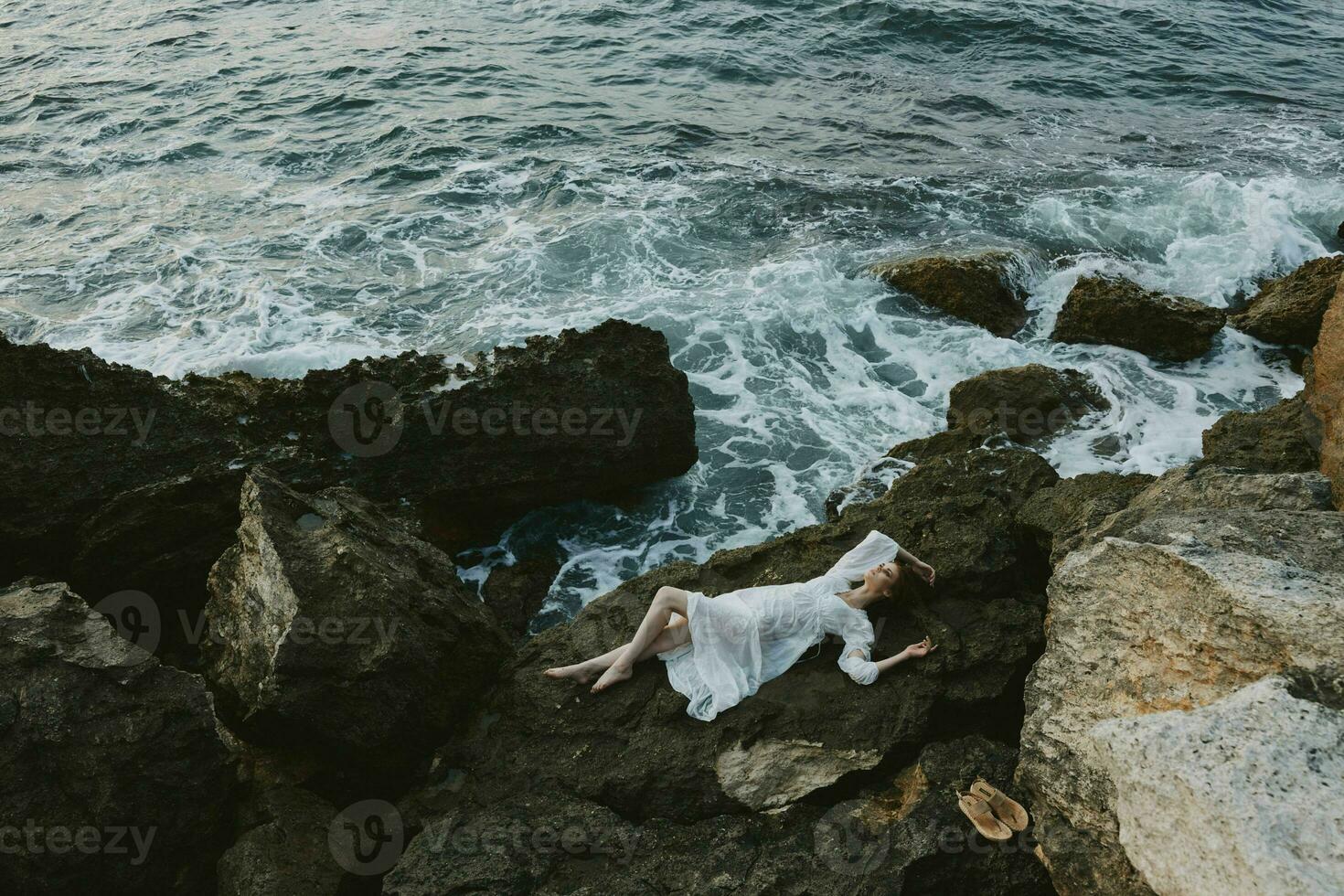 Frau im ein abgelegen Stelle auf ein wild felsig Küste im ein Weiß Kleid Aussicht von über foto