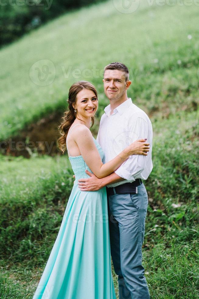 Ein glücklicher Kerl in einem weißen Hemd und ein Mädchen in einem türkisfarbenen Kleid gehen im Waldpark spazieren foto