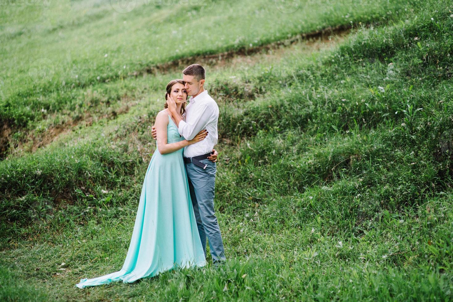 Ein glücklicher Kerl in einem weißen Hemd und ein Mädchen in einem türkisfarbenen Kleid gehen im Waldpark spazieren foto