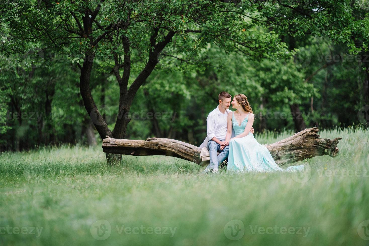 Ein glücklicher Kerl in einem weißen Hemd und ein Mädchen in einem türkisfarbenen Kleid gehen im Waldpark spazieren foto