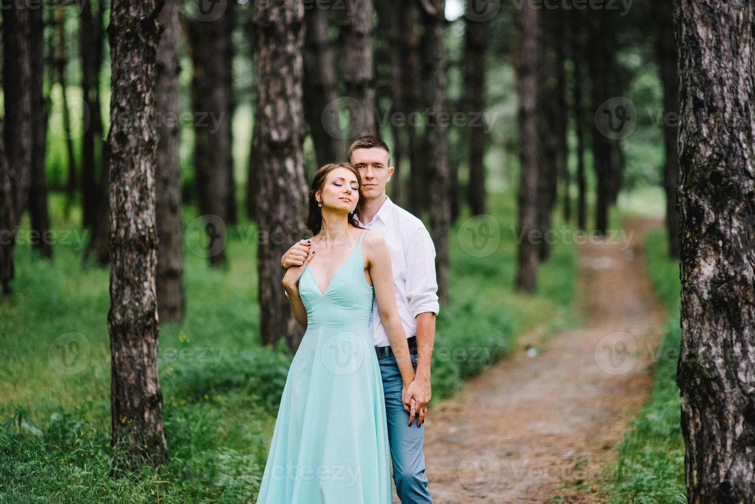 Ein glücklicher Kerl in einem weißen Hemd und ein Mädchen in einem türkisfarbenen Kleid gehen im Waldpark spazieren foto