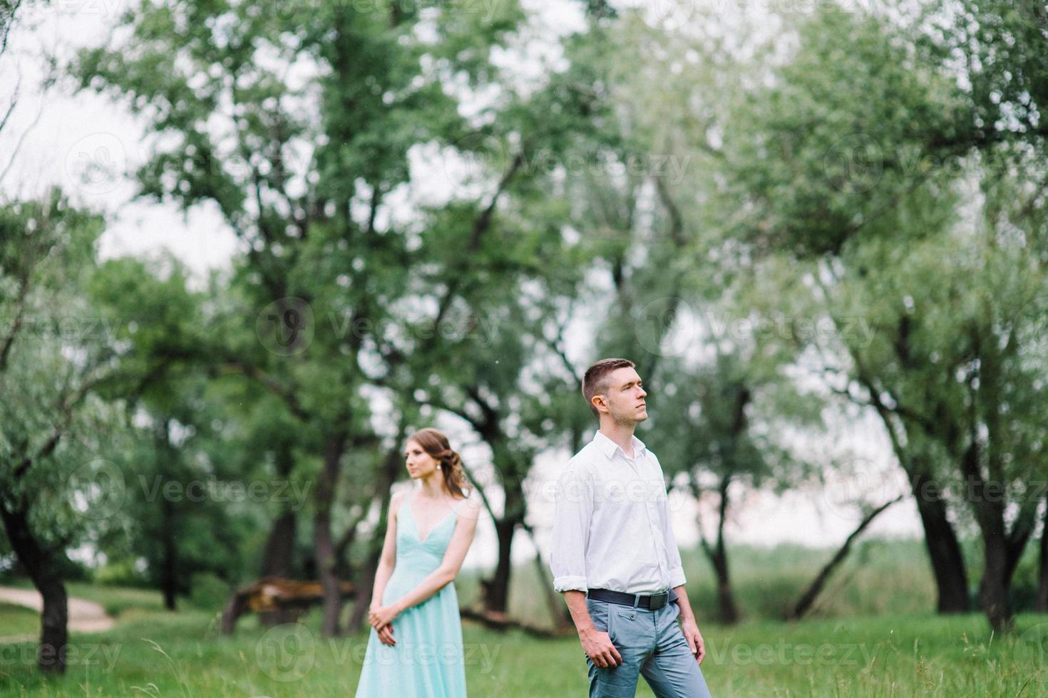 Ein glücklicher Kerl in einem weißen Hemd und ein Mädchen in einem türkisfarbenen Kleid gehen im Waldpark spazieren foto