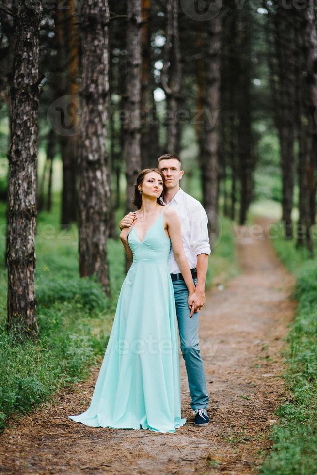 Ein glücklicher Kerl in einem weißen Hemd und ein Mädchen in einem türkisfarbenen Kleid gehen im Waldpark spazieren foto