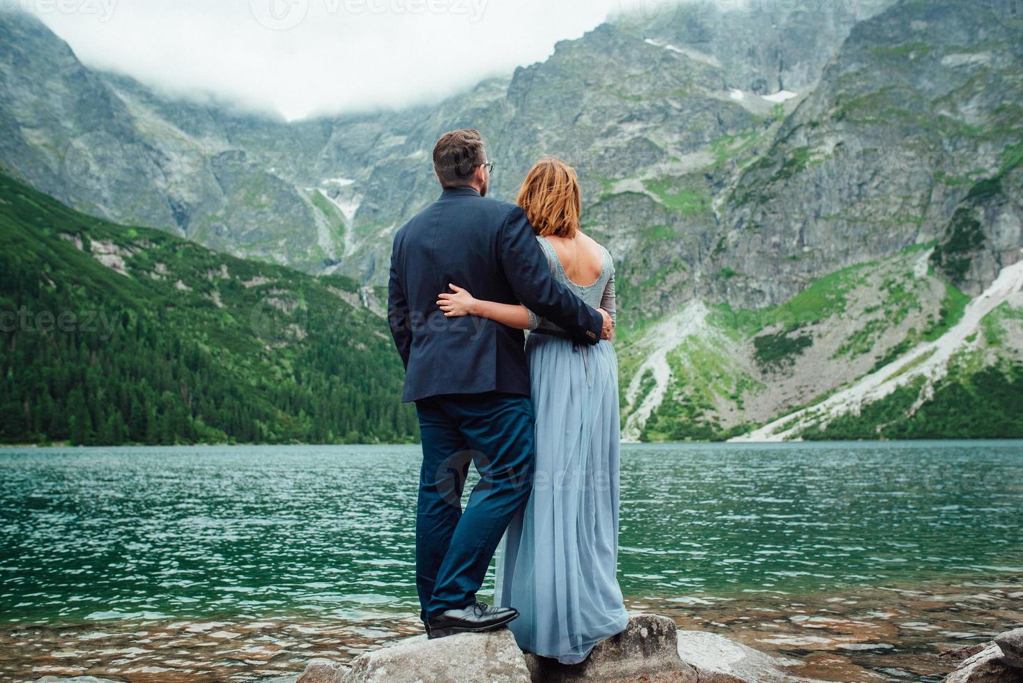 junges Paar auf einem Spaziergang in der Nähe des Sees, umgeben von den Bergen foto