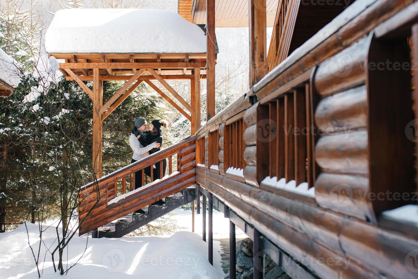 ein paar junge Leute, ein Mann und ein Mädchen auf der Veranda eines schneebedeckten Holzhauses foto