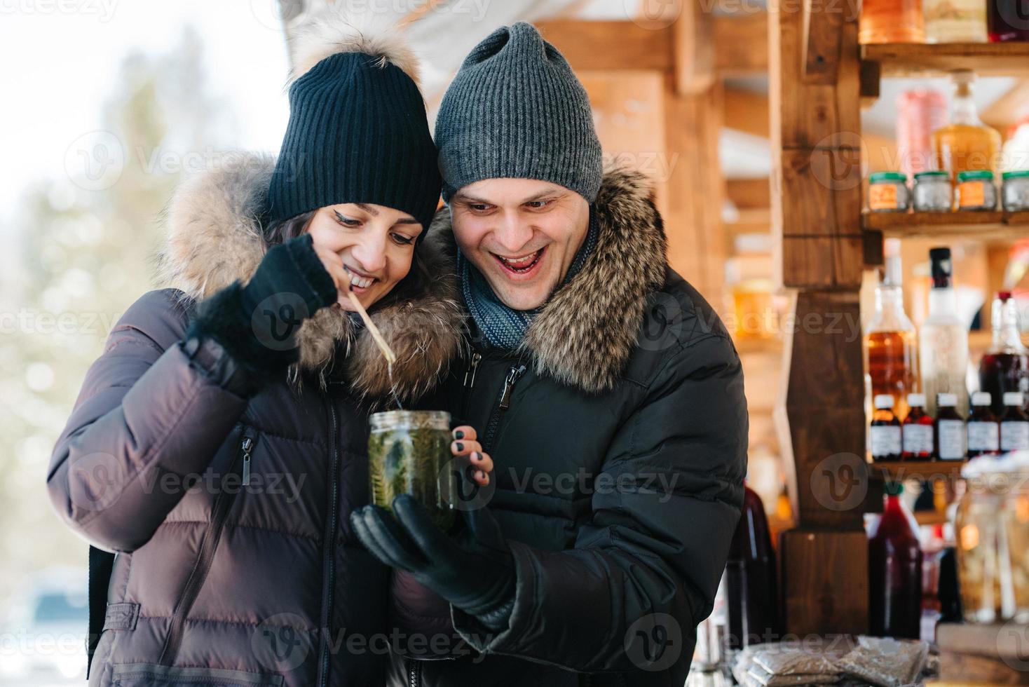 freudiges Mädchen und Kerl in warmer Winterkleidung auf dem Markt versuchen Honig foto