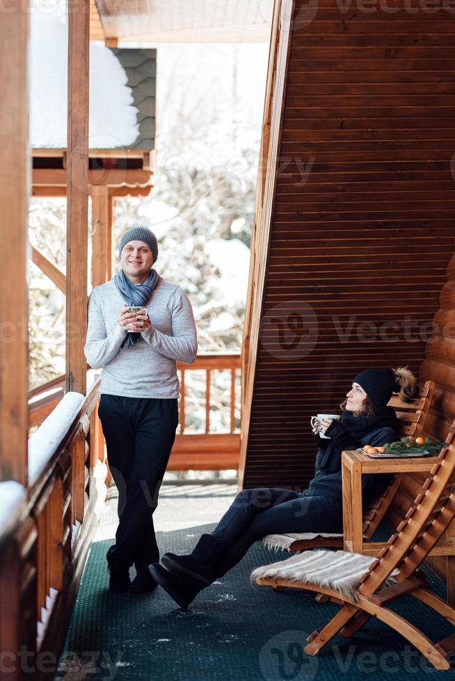 ein paar junge Leute, ein Mann und ein Mädchen auf der Veranda eines schneebedeckten Holzhauses foto