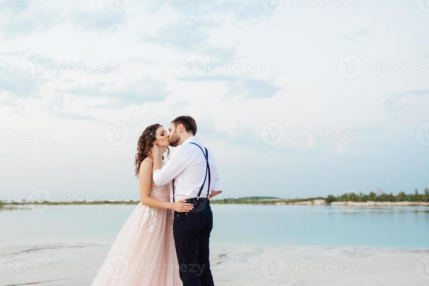 Ein junges Paar, ein Mann in einer schwarzen Reithose und ein Mädchen in einem rosa Kleid, gehen den weißen Sand entlang foto