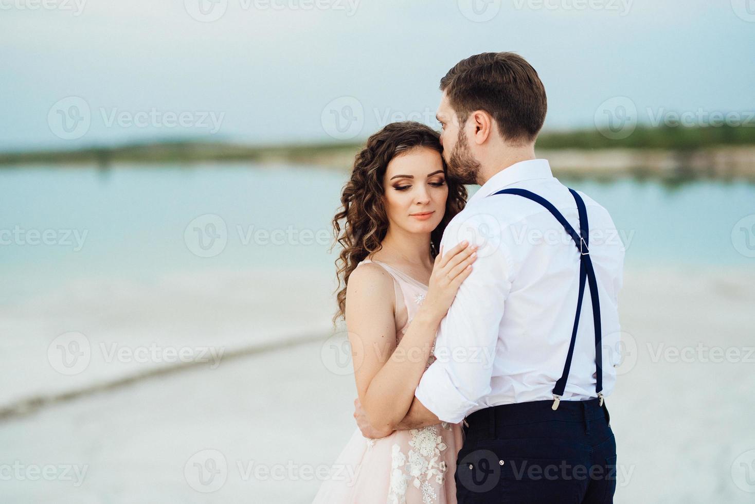 Ein junges Paar, ein Mann in einer schwarzen Reithose und ein Mädchen in einem rosa Kleid, gehen den weißen Sand entlang foto