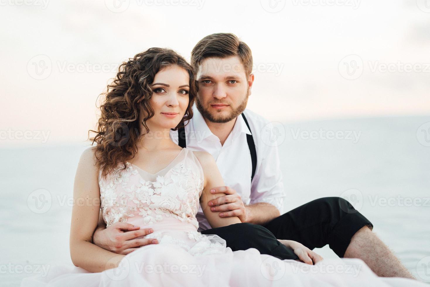 Ein junges Paar, ein Mann in einer schwarzen Reithose und ein Mädchen in einem rosa Kleid, gehen den weißen Sand entlang foto