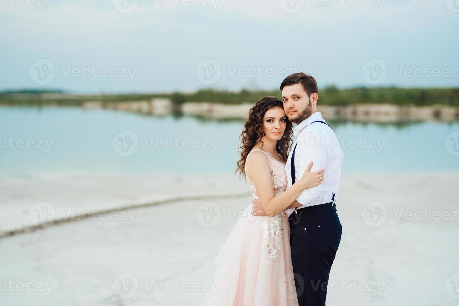 Ein junges Paar, ein Mann in einer schwarzen Reithose und ein Mädchen in einem rosa Kleid, gehen den weißen Sand entlang foto