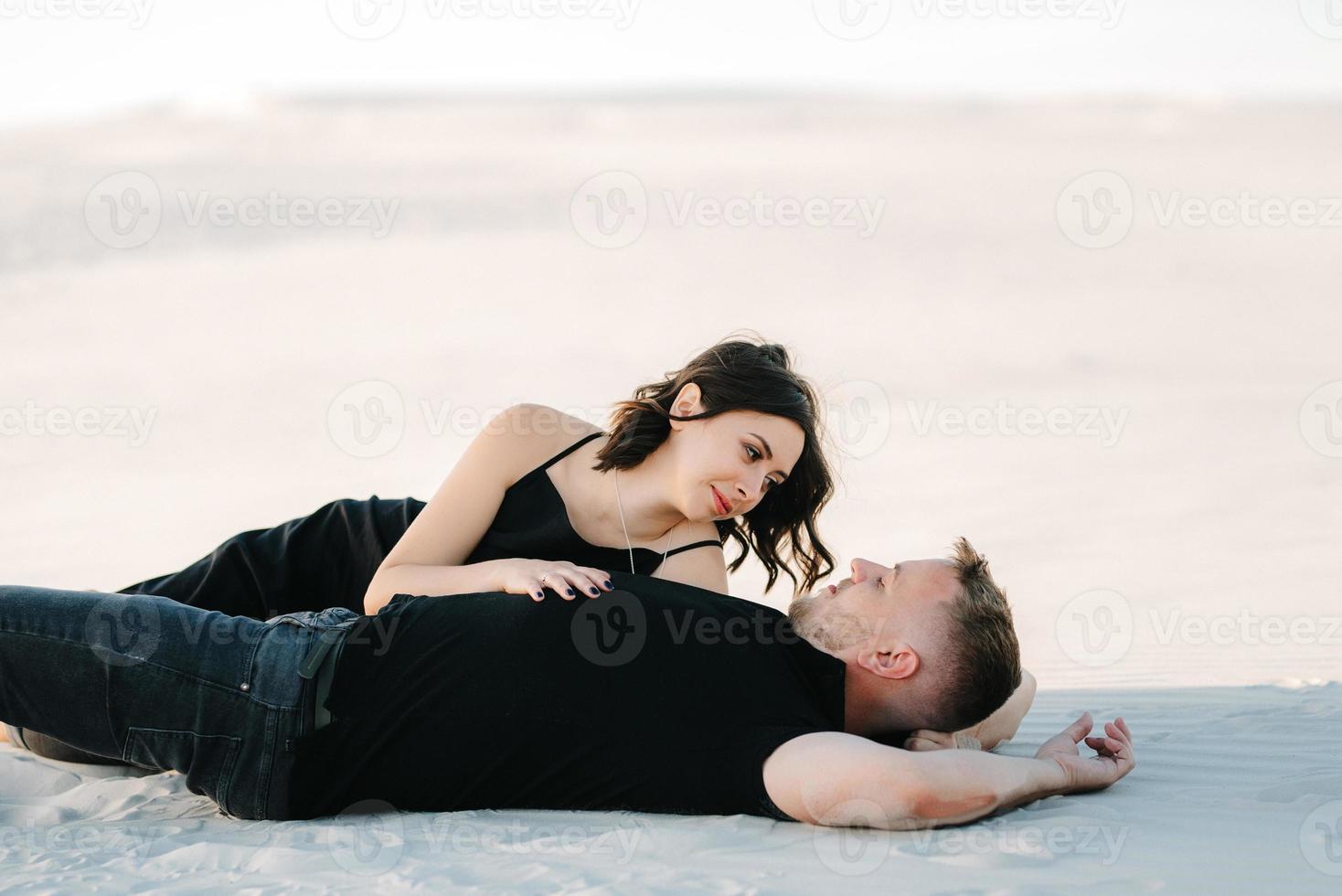junges Paar ein Mann und ein Mädchen mit freudigen Gefühlen in schwarzen Kleidern gehen durch die weiße Wüste foto