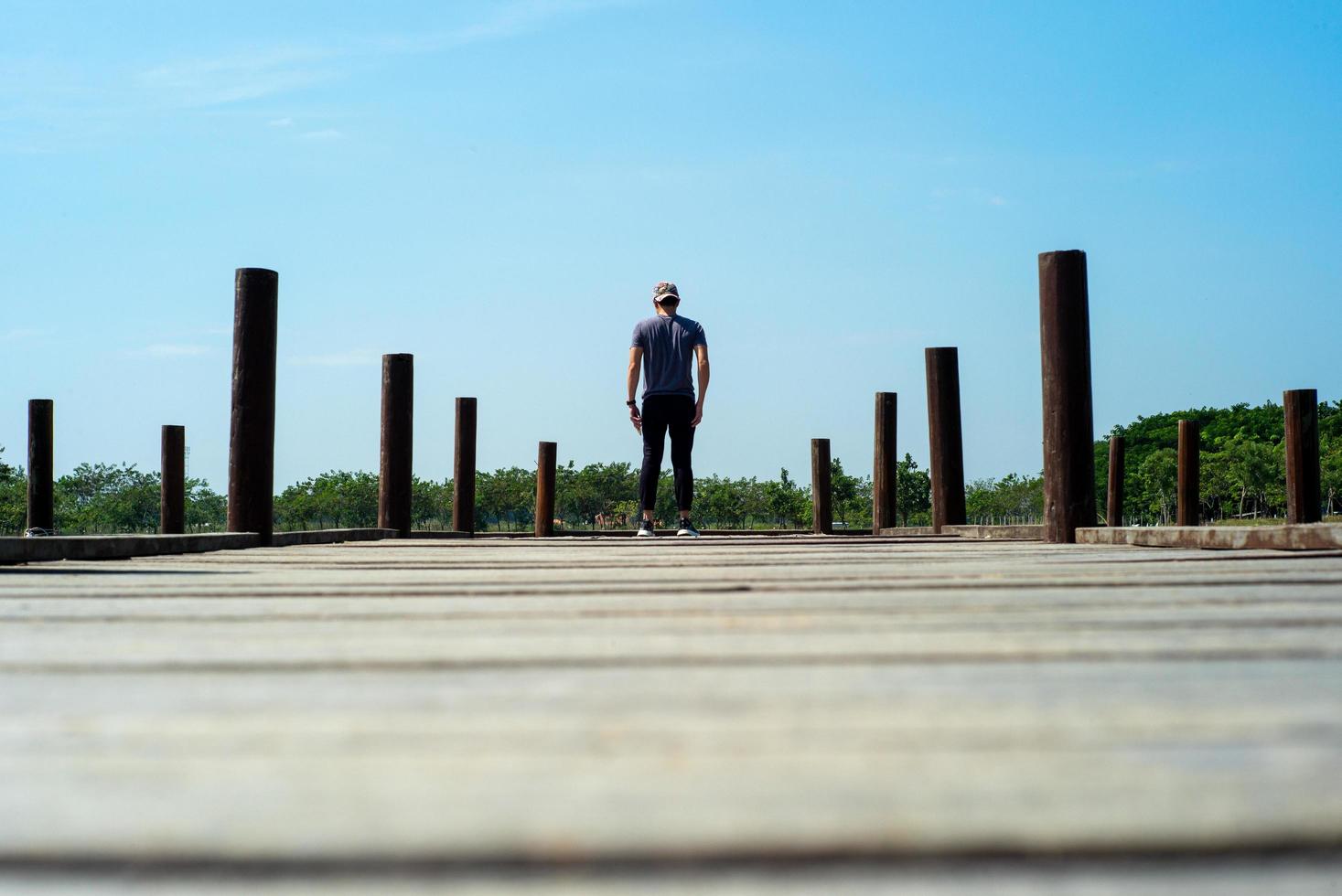 Hinteres Porträt des gutaussehenden Mannes im lässigen Stoff steht auf Holzbrücke mit blauem Himmelhintergrund foto