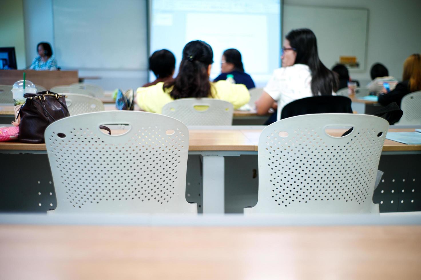 Selektiver Fokus auf eine Reihe leerer Stühle mit einer verschwommenen Gruppe von Studenten im Hintergrund foto