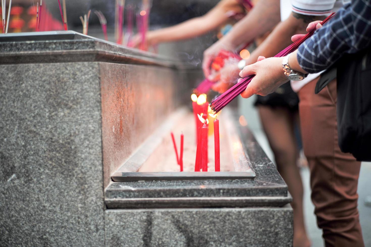 Nahaufnahme Hände halten das Bündel von Weihrauch zum Anzünden mit Kerzen in der Sandschale foto