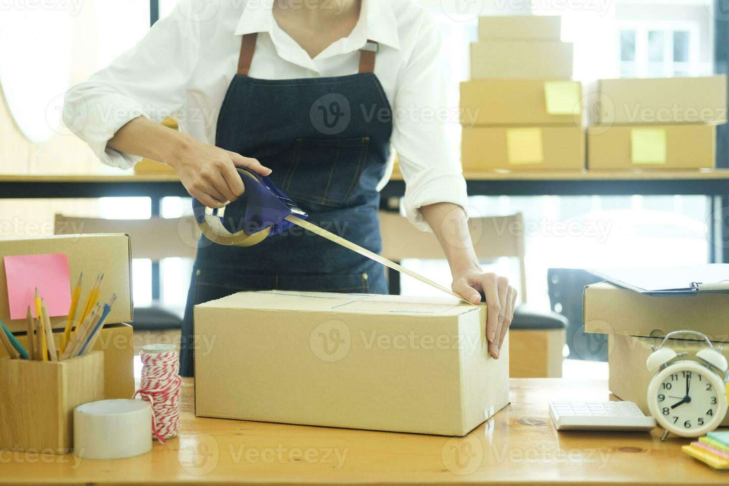 asiatisch weiblich Kleider Geschäft Inhaber falten ein T-Shirt und Verpackung im ein Karton Paket Kasten. foto