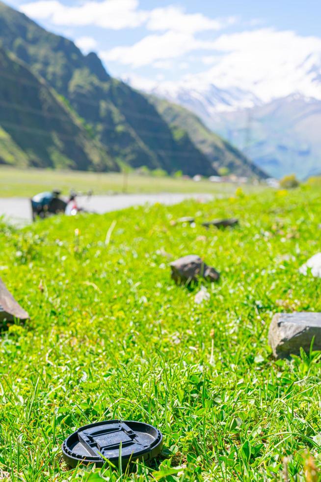 Objektivdeckel im Gras mit Bergen foto