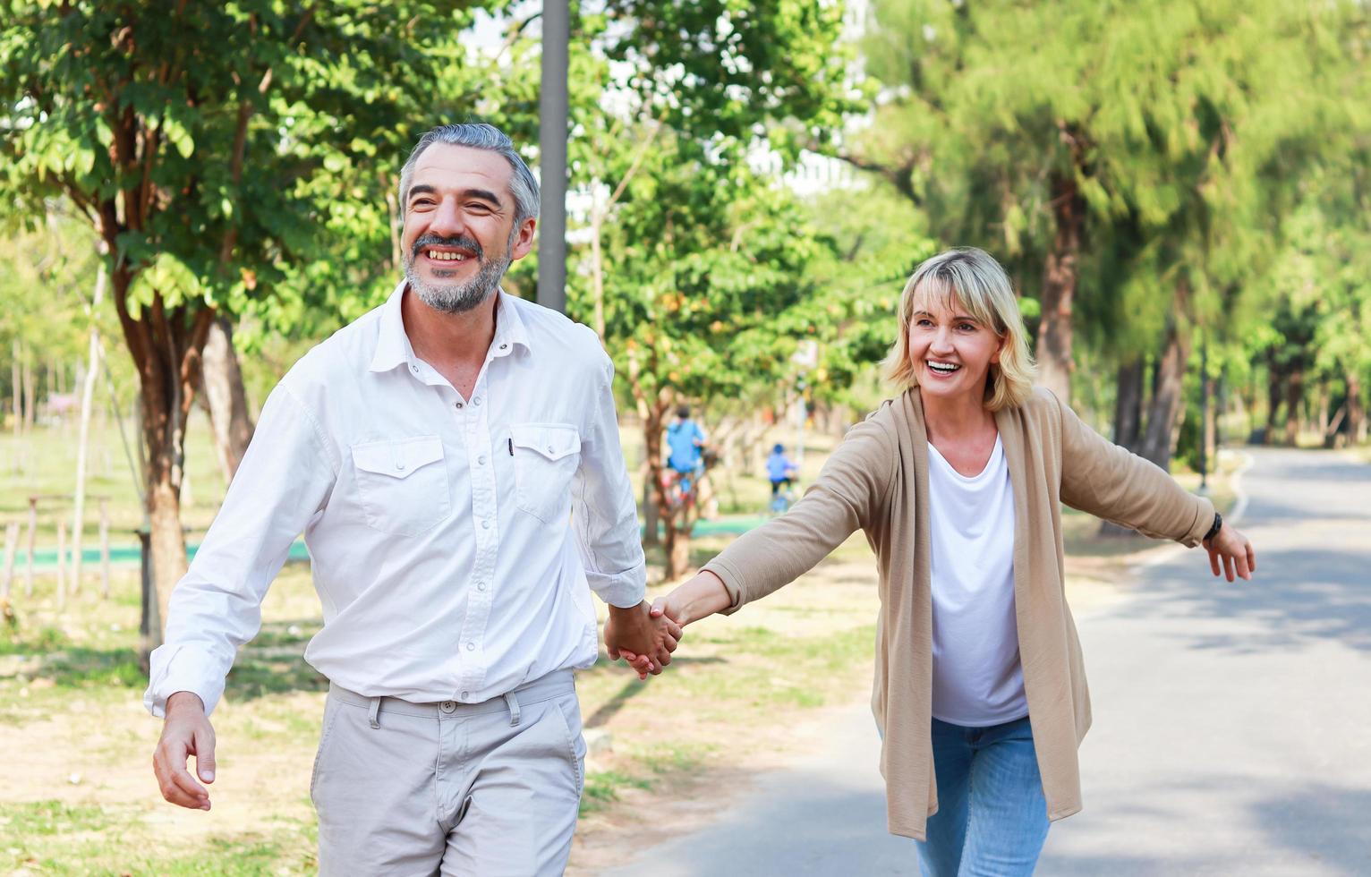 älteres kaukasisches Ehepaar, das Hand in Hand in einem Park mit Liebe geht. Konzept für einen schönen Urlaub foto