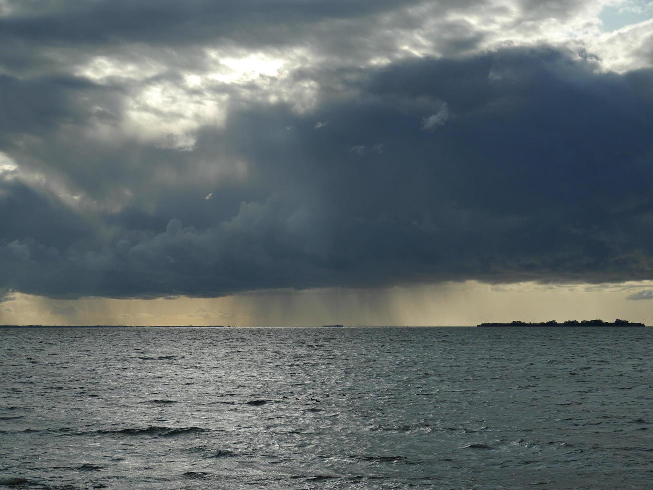 riesige schwarze Wolke gießt Regen auf das Meer foto