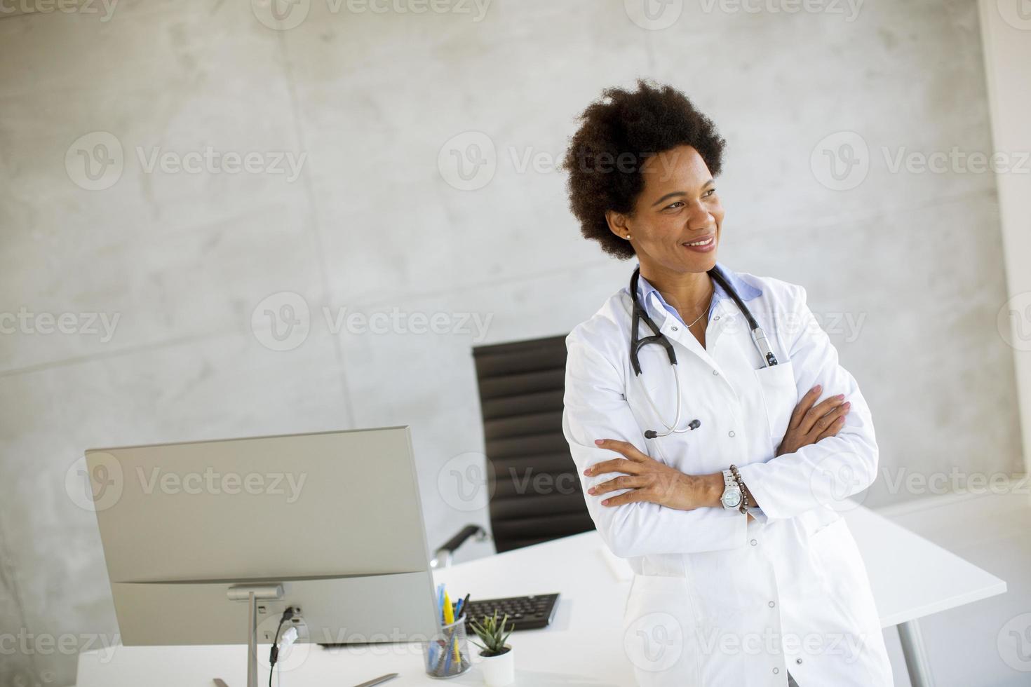 Arzt mit verschränkten Armen vor einem Schreibtisch foto