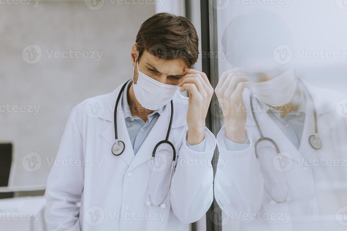 Arzt in Maske an ein Fenster gelehnt foto