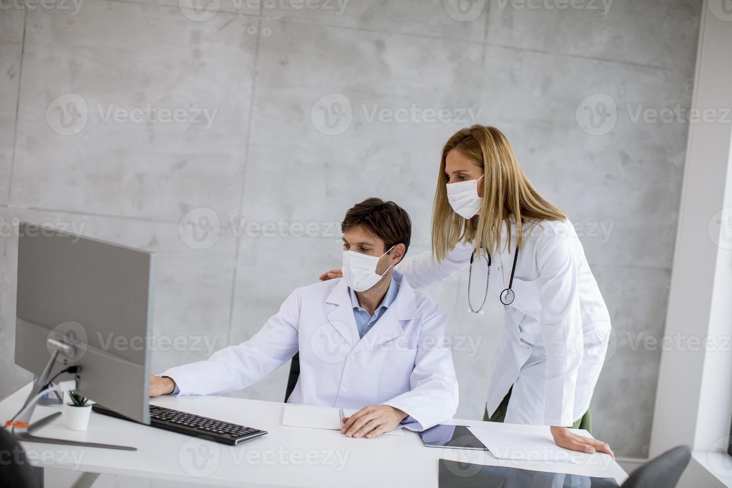 zwei Ärzte, die einen Computer in Masken betrachten foto
