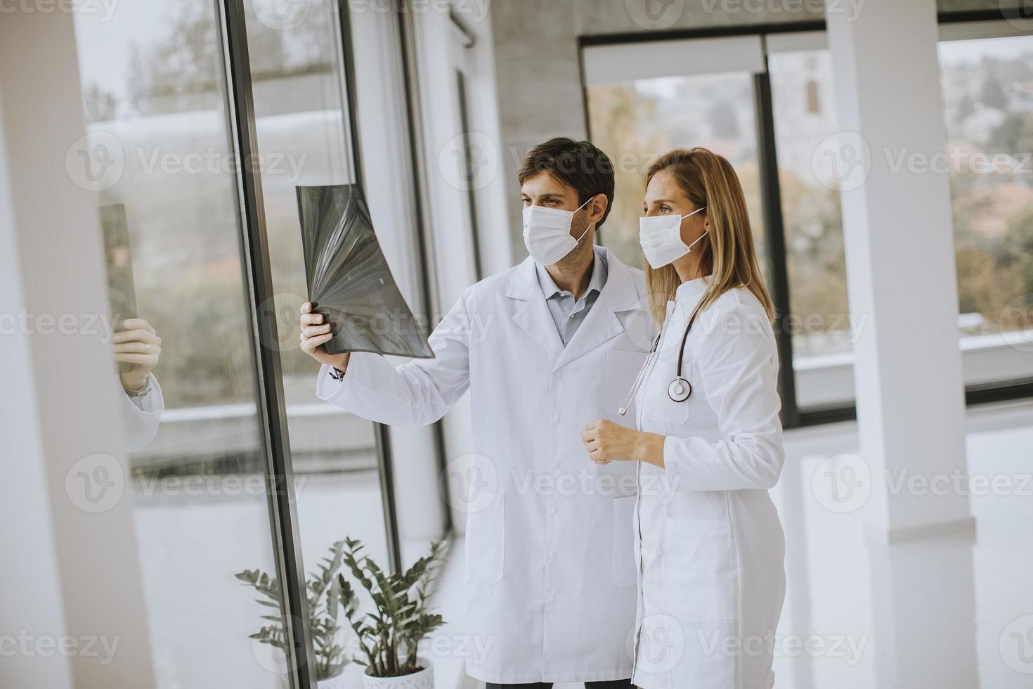 zwei Ärzte in Masken, die eine Röntgenaufnahme halten foto